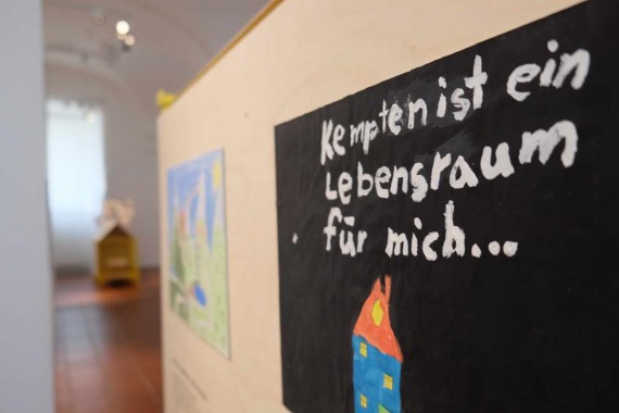 Stellwand aus Holz mit Kinderbildern. Bild im Vordergrund mit Text: Kempten ist ein Lebensraum für mich.
