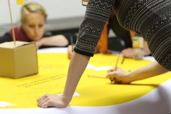 Ideen-Tisch: Junge Frauen bäugen sich über Tisch mit gelber Papiertischdecke und beschreiben sie 