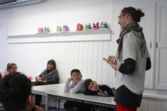 Im Klassenzimmer: Kinder lümmeln gemütlich auf Schulbänken und blicken gespannt auf Kathrin Seckinger, hinten sitzt lachend die Lehrerin 