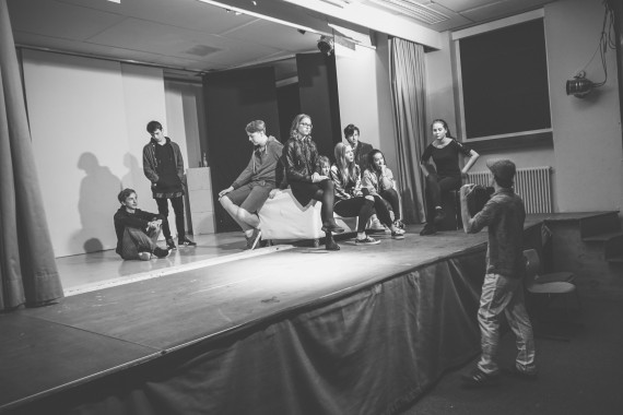 Theaterprobe: Schülergruppe agiert auf Bühne; davor gibt Norman Graue Anweisungen