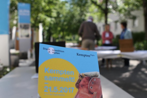 Flyer &quot;Kempten sammelt&quot; 21.5.2017, im Hintergrund Menschengruppe an Tischen vor dem Alpin-Museum
