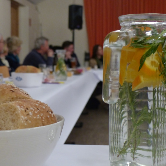 Gedeckter Tisch, im Vordergrund: Wasserkaraffe mit Orangenscheiben und Kräutern