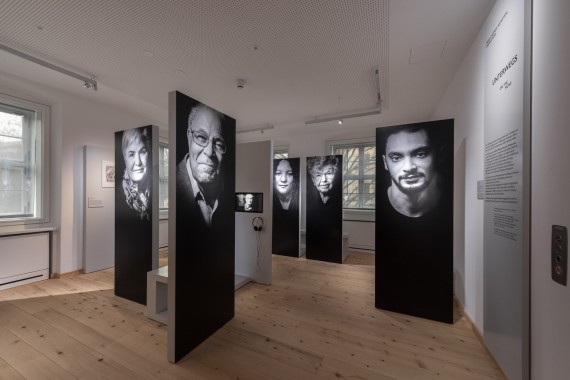 Schwarze Stehlen mit großen Schwarz-Weiß-Portraitfotos mit Hörstationen im Raum &quot;Migration&quot;