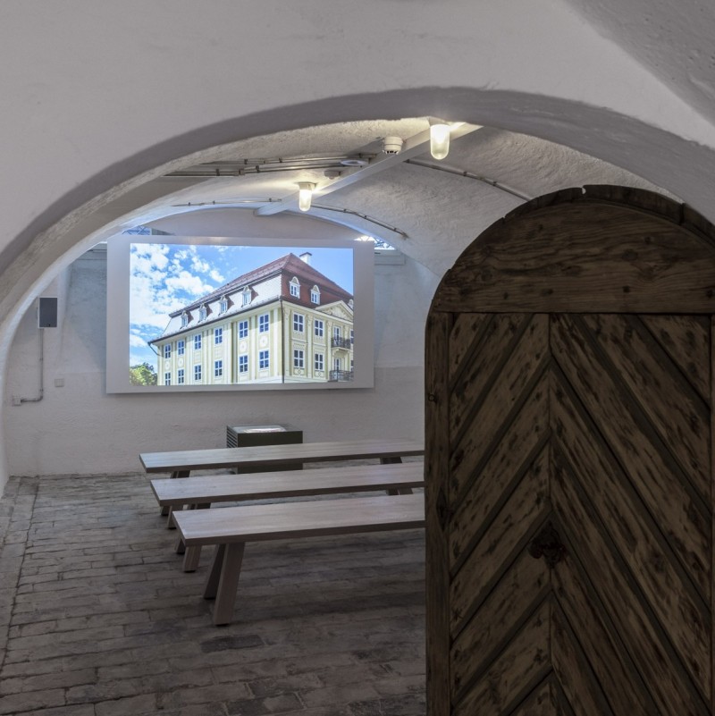 Blick in den kleinen rustikalen Kino-Raum im Gewölbekeller des Kempten-Museums mit Leinwand, Holzbänken und gepflastertem Steinboden