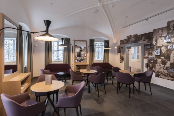 Museumscafé: runde Tische mit modernen lilanen Sesselstühlen. An der Wand: Bilder (monochrom) von Kemptener Persönlichkeiten