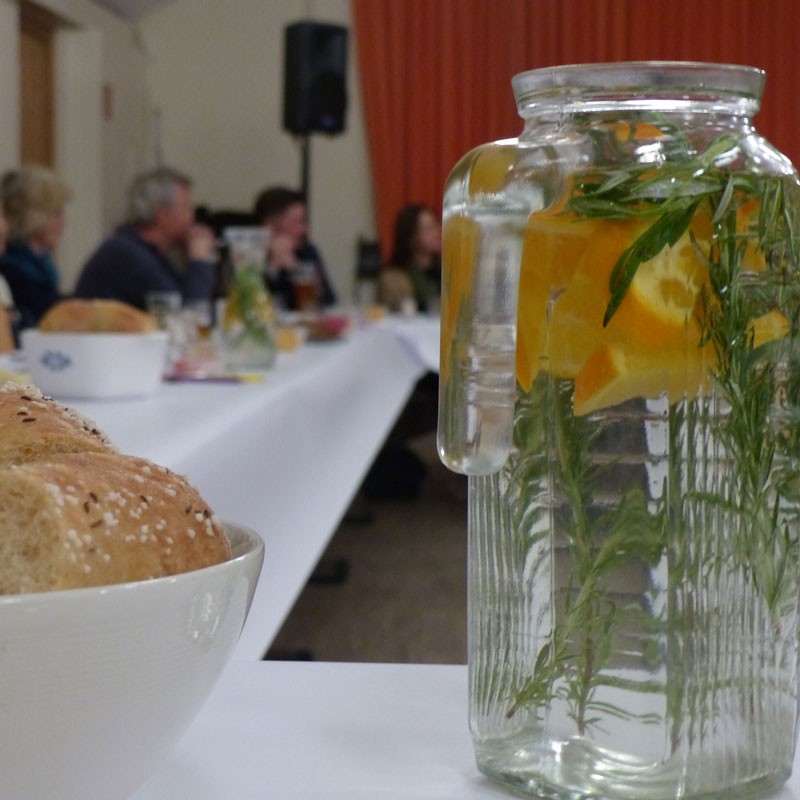 Gedeckter Tisch, im Vordergrund: Wasserkaraffe mit Orangenscheiben und Kräutern 