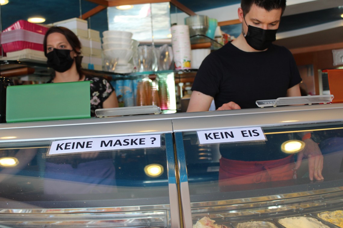 Zwei Eisverkäufer mit schwarzen Masken hinter Eistheke mit Aufschrift &quot;Keine Maske? Kein Eis!&quot;