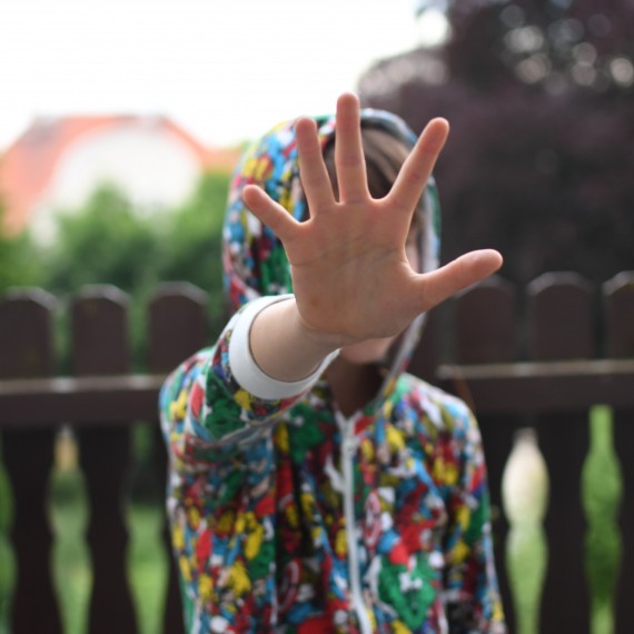 Kind mit Stop-Geste: ausgestreckter Arm mit Hand vor Gesicht
