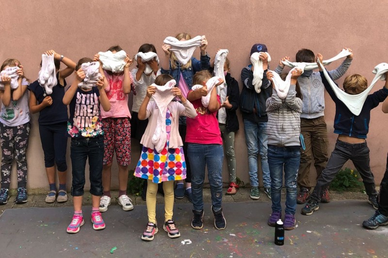 Kinder vor Mauer, die selbst hergestellten Schleim vor ihre Gesichter halten