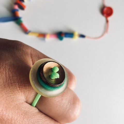 Hand mit DIY-Ring aus grünem Gummiband und Knöpfen in Grüntönen und Gold