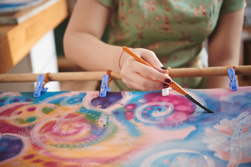 Mädchen bemalt ein Seidentuch mit bunten Farben und kreisförmigen Mustern