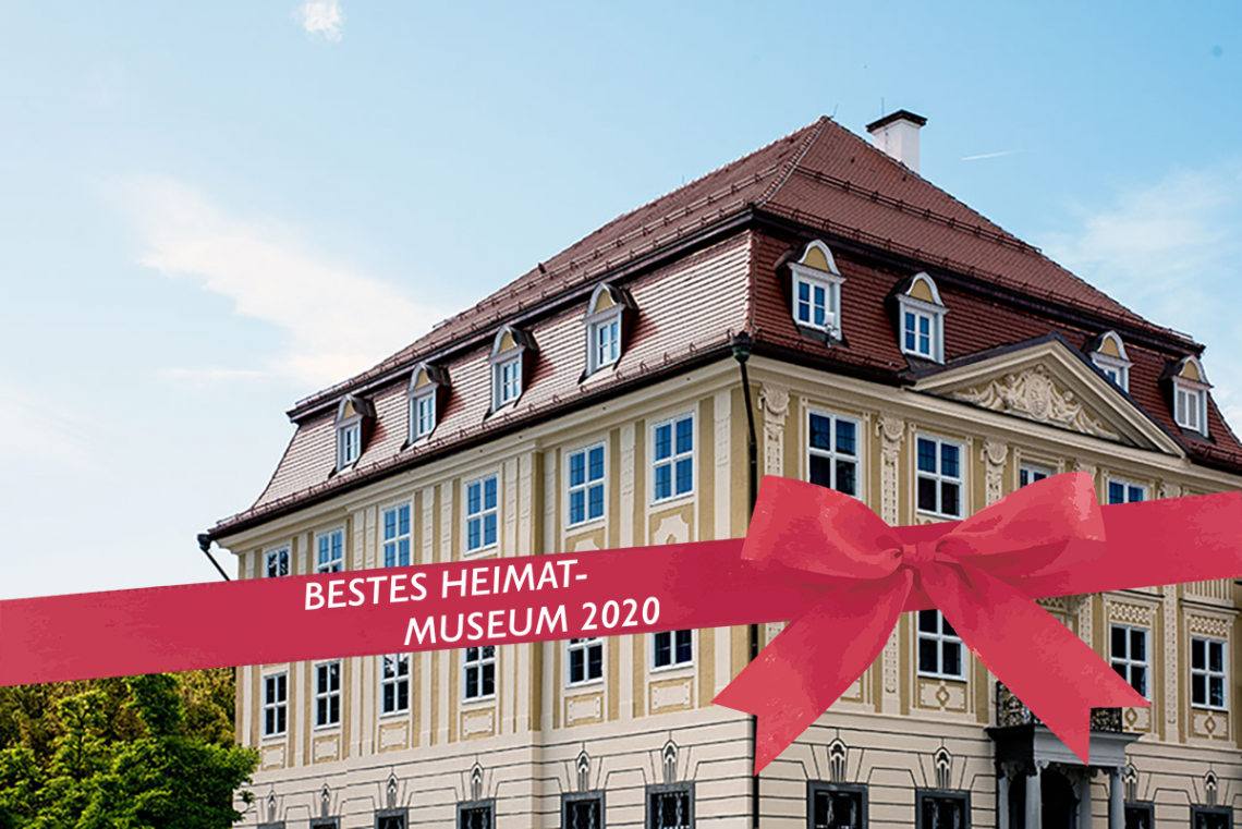 Kempten-Museum (Zumsteinhaus: historisches gelbes Gebäude mit Sprossenfenstern und Walmdach) mit roter Schleife (Text: Bestes Heimatmuseum 2020)