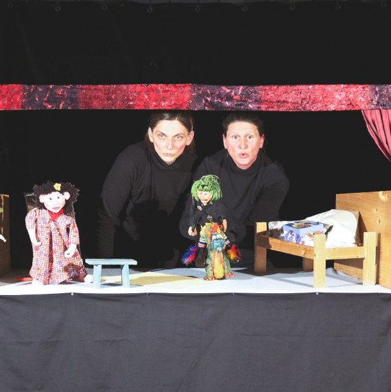 Zwei schwarz gekleidete Puppenspielerinnen mit Puppentheater