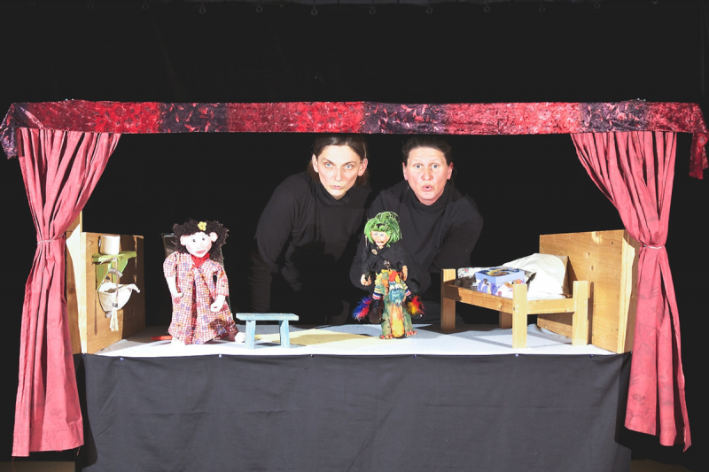Zwei schwarz gekleidete Puppenspielerinnen mit Puppentheater
