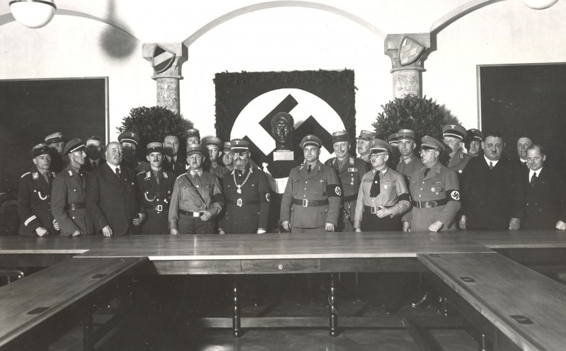 Männer in Uniform stehen vor einer Hakenkreuzfahne