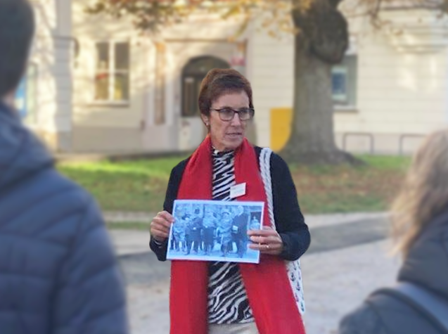 Stadtführerin zeigt Menschengruppe Schwarz-Weiß-Foto