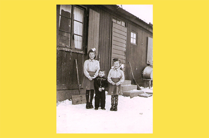 schwarz-wei&szlig; Foto mit drei Kindern vor einem Holzhaus
